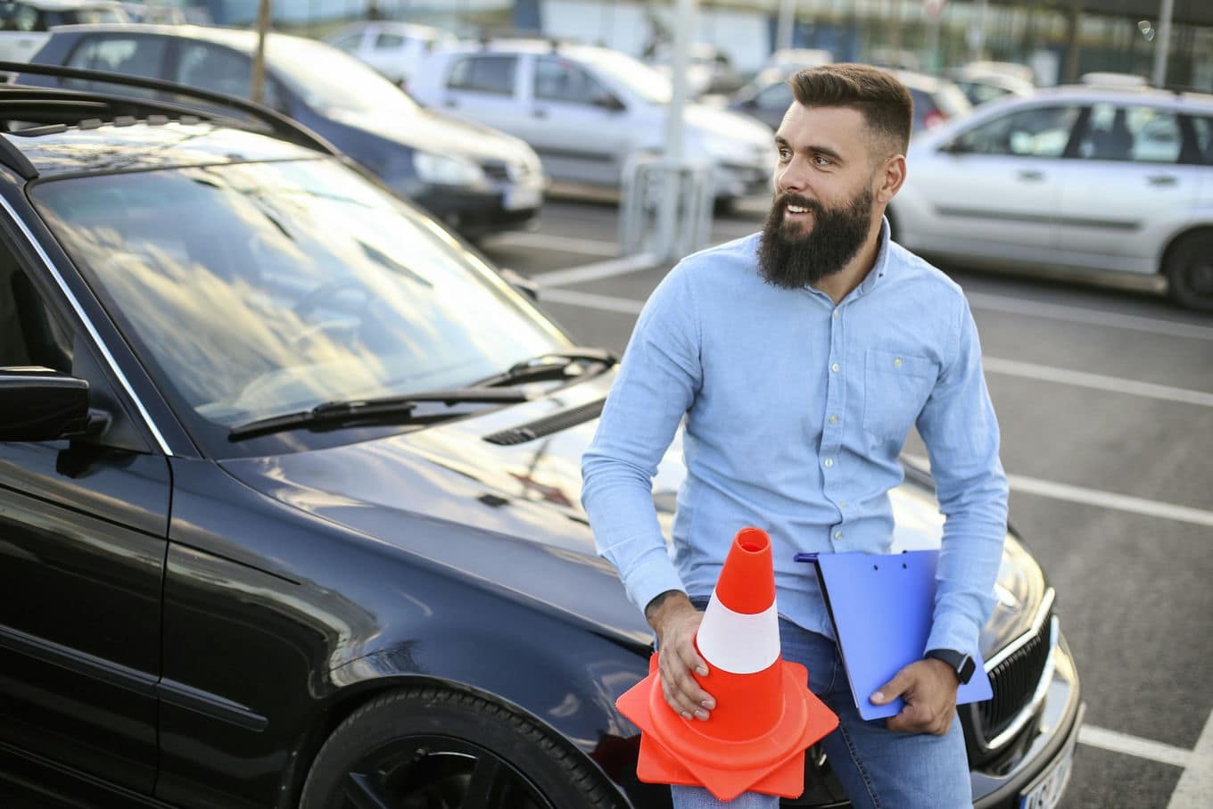 mężczyzna siedzący na masce samochodu i trzymający pachołek drogowy